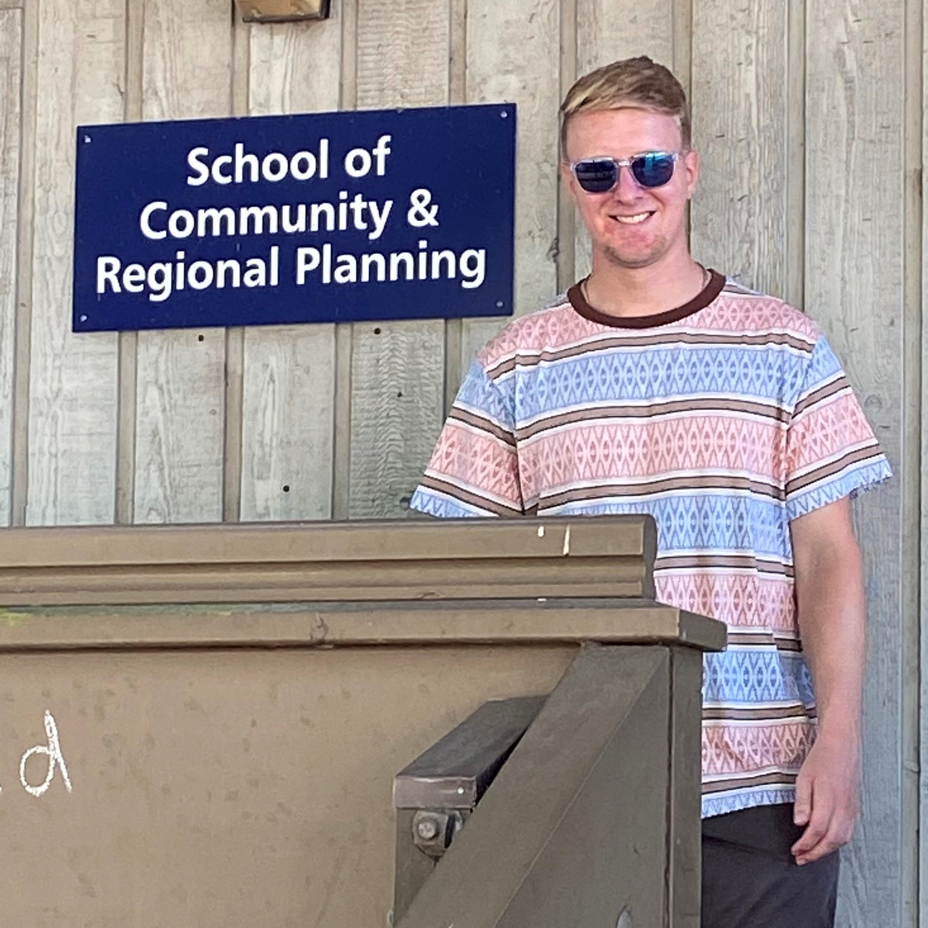 Man in sunglasses and T-shirt beside SCARP building sign