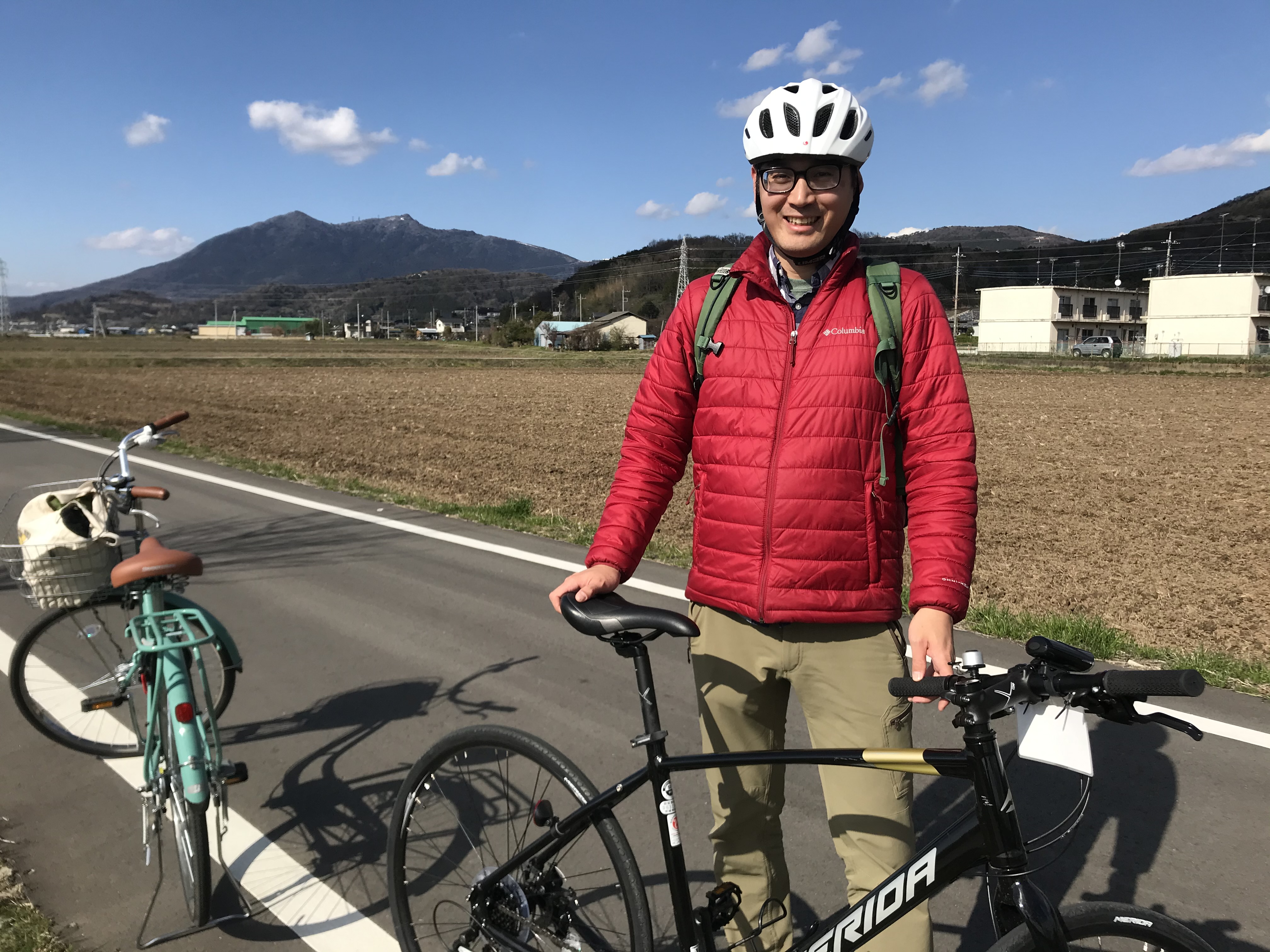 Tadayori beside his bicycle, along a long road among grassl cycle route