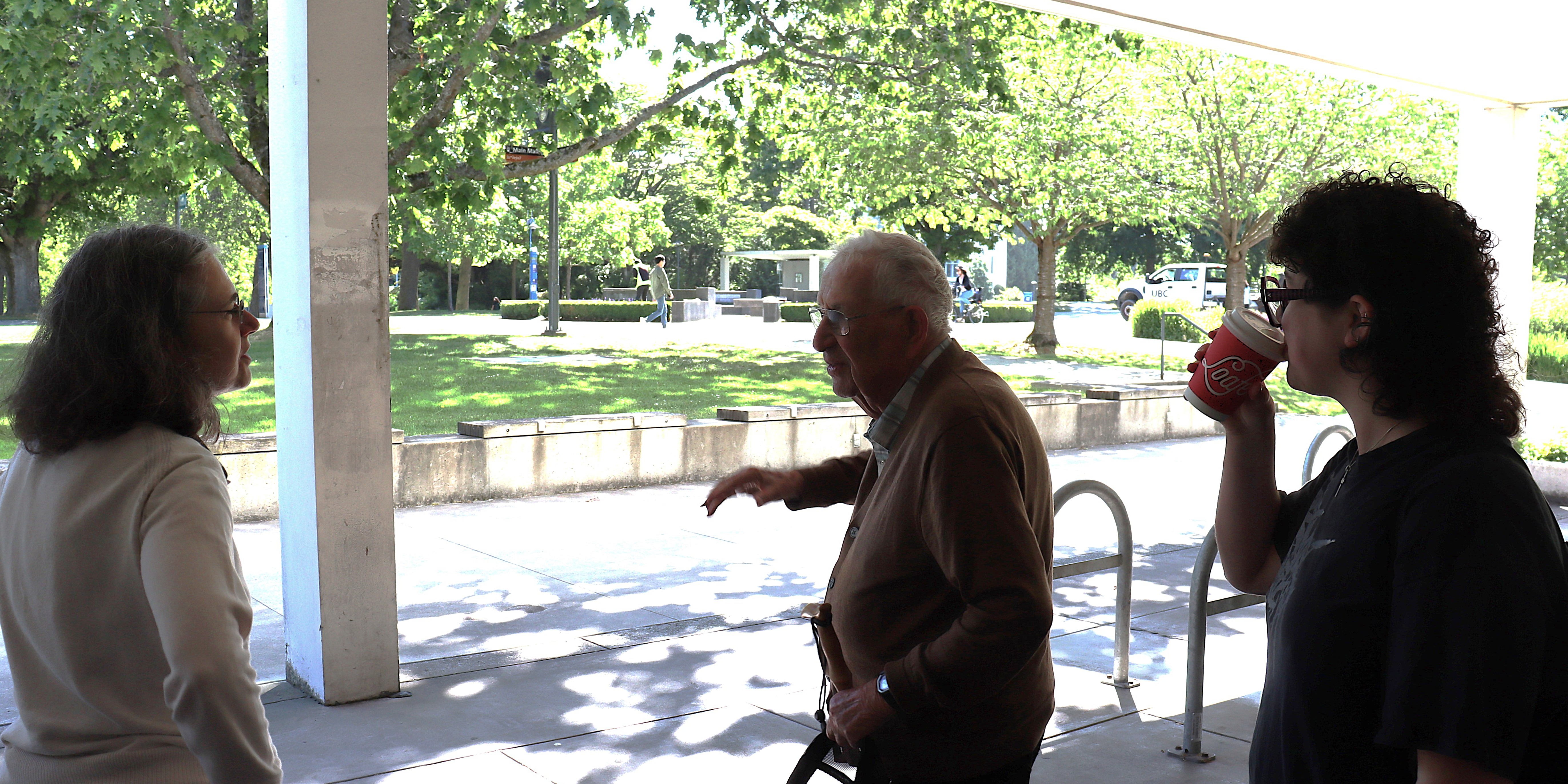 Three people talking by support pillars by foliage-laden walkway