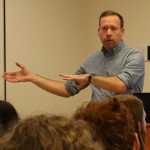 Man with rolled-up sleeves, gesturing as he speaks to students