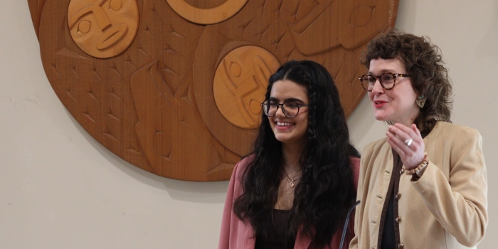 Women presenting beside a Musqueam symbol