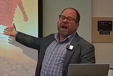 Man in grey blazer indicating projected screen