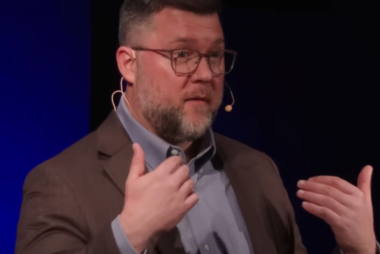 Man in suit addressing audience on TED-Talk stage