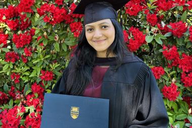 Woman in regalia among roses holding UBC diploma