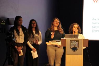 Student at UBC lectern, gesturing to 3 peers