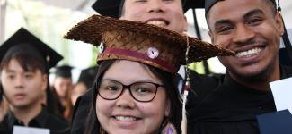 several graduates in regalia, one of them in custom Indigenous woven mortar-board