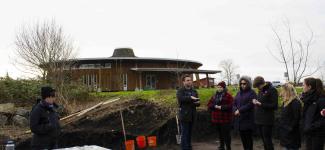 Several students listening to an Indigenous man outside a round building
