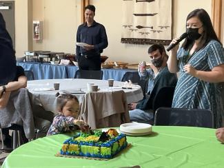 Jessie talking into mic while little girl fingers freshly presented cake