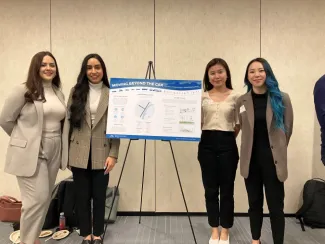 Four young women posing beside a project poster