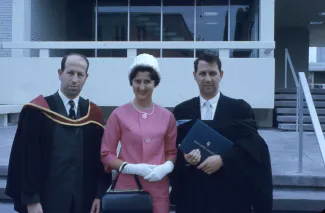 An old picture with two men in graduation regalia and a woman in 1960s-style outfit