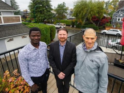 Three researchers pose on a wood patio in a neighbourhood