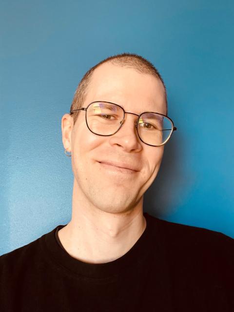 Smiling person with glasses and cropped hair