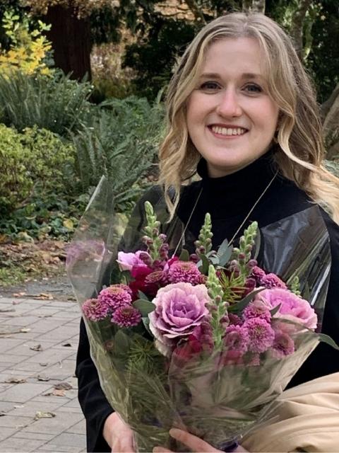 A woman among a bush-laden path holding a bouquet of flowers