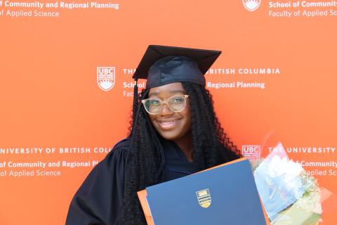 Savonnaé, in regalia holding flowers and diploma, in front of SCARP logo