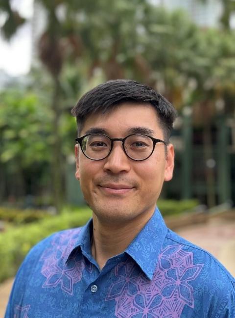 Man in glasses and blue patterned shirt, among green pathway