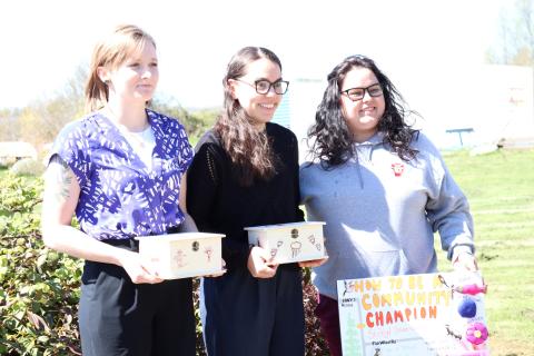 Three people hold up "How to be a community champion" poster