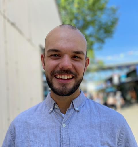 Bearded man outside near white-stoned wall, tree