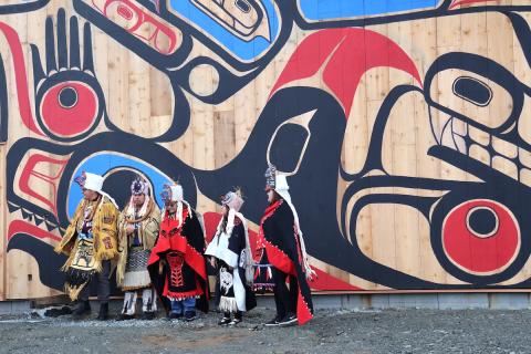 People in Indigenous regalia in front of mural