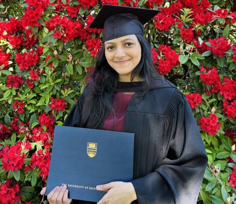 Woman in regalia among roses holding UBC diploma