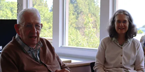 A man and a woman sitting at a table, trees and sunshine in the background