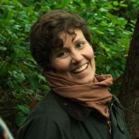 A woman with short hair in a scarf, outside among trees