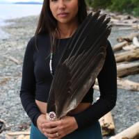 Indigenous woman on beach holding object made of bird's wing